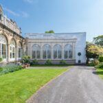 A large building under construction, covered by a wrap depicting a greenhouse