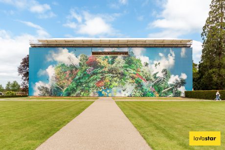 A building wrap depicting lush, colorful foliage against a blue sky